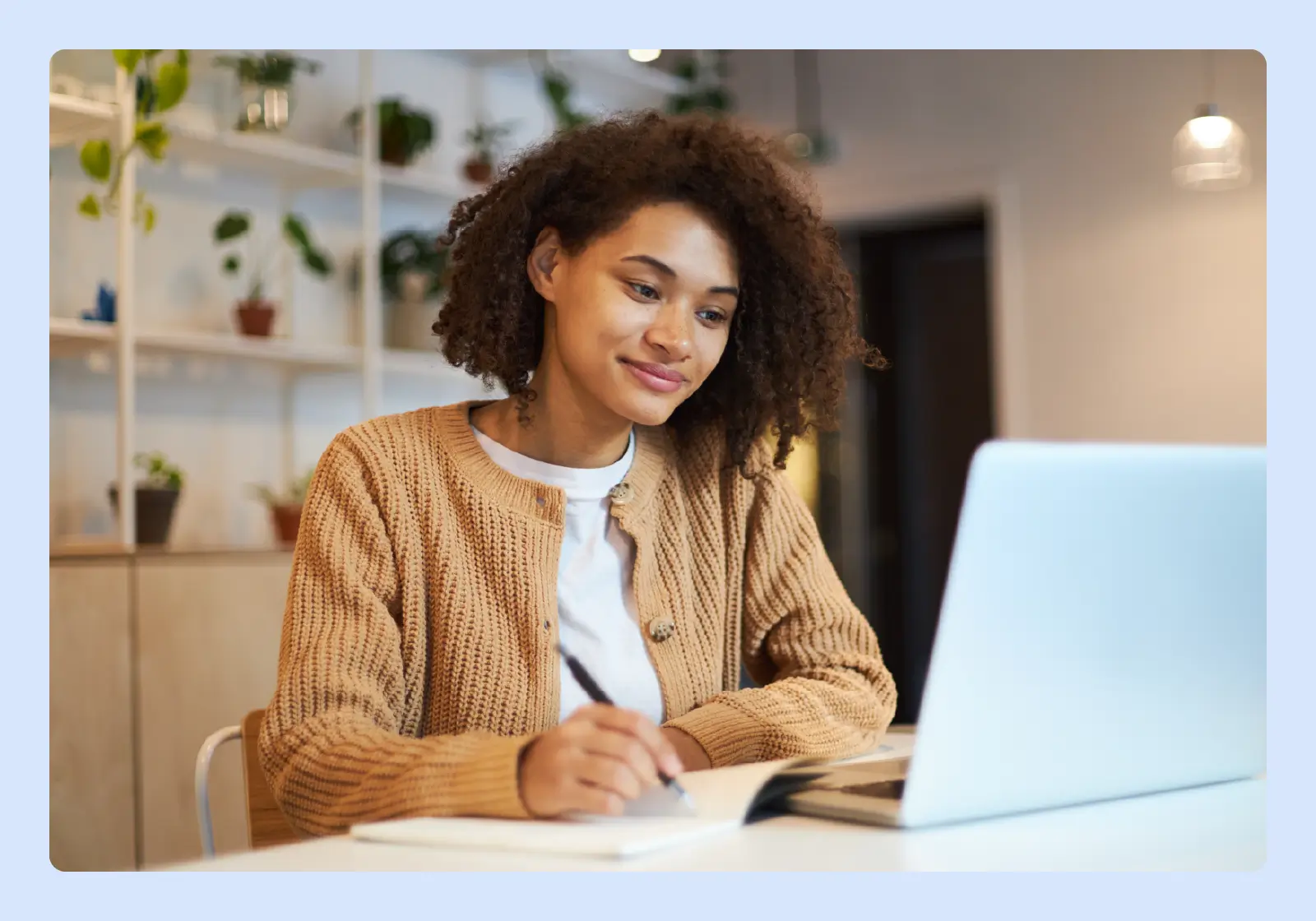 a woman is noting something down in her notebook and her laptop is in front of her